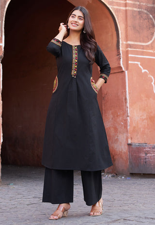 Woman wearing a black traditional outfit with embroidery in front of an archway.
