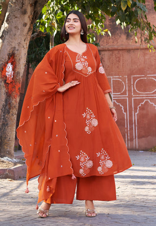 Woman in an orange embroidered outfit standing outdoors with a tree and wall in the background