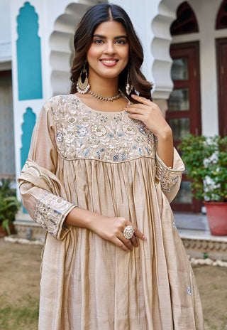 A woman wearing a beige embroidered kurta with floral embroidery on the chest and sleeves, standing outdoors in front of a white building with arches.