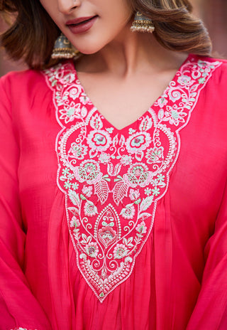 A close-up of a woman wearing a bright pink traditional embroidered top or kurta with a large white floral embroidery panel on the chest and neckline.