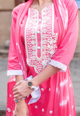 A close-up of a woman wearing a bright pink traditional outfit with white floral embroidery and lace trim, along with a matching sheer pink dupatta.
