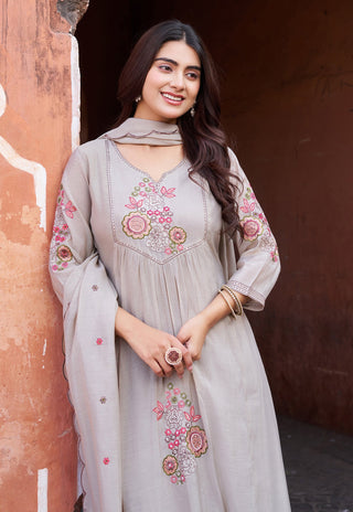 Woman wearing a light gray embroidered dress standing against a textured wall.