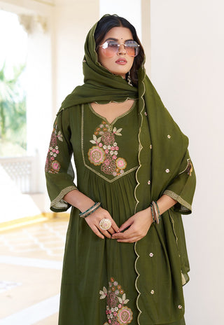 Woman wearing a green embroidered dress with a matching headscarf indoors.