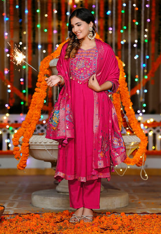 A woman models a bright magenta pink ethnic salwar kameez suit with a matching dupatta. The ensemble features intricate multicolor embroidery on the chest and a heavily embellished border, styled with a matching pink trouser set.