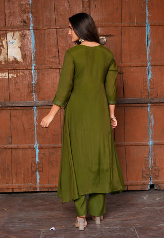 A woman wearing an olive green three-piece kurta set, shown from the back against a rustic reddish-brown wooden door.