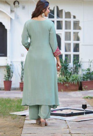 A woman wearing a sage green three-piece kurta set with matching pants, shown from the back in an outdoor courtyard setting.
